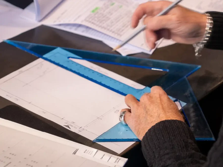 Mani che tracciano un disegno tecnico con squadra blu su tavole di progetto