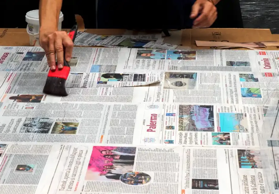 Mani che verniciano con pennello rosso un pezzo su un piano coperto di giornali