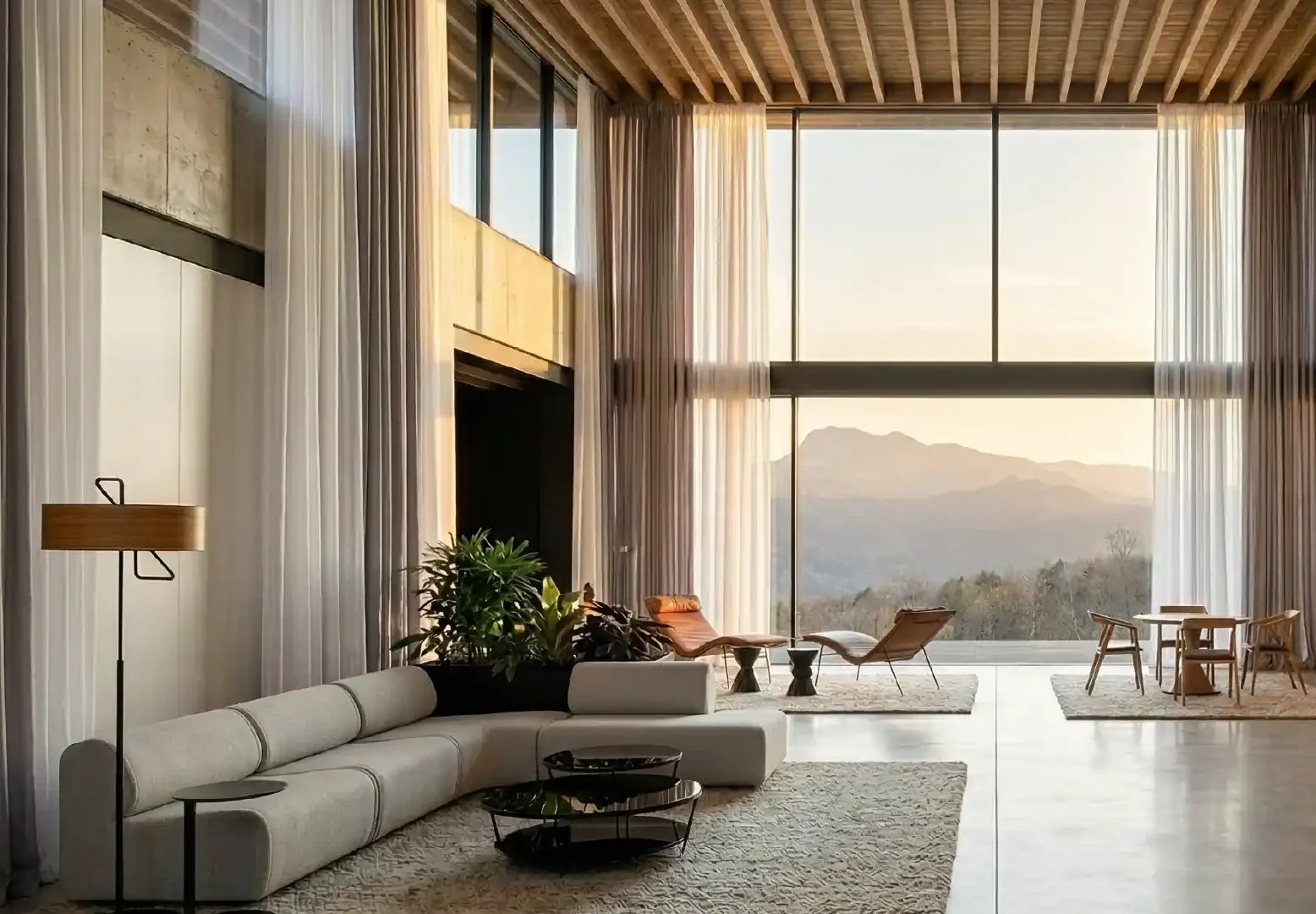 Lounge a doppia altezza con divano lineare e grandi vetrate affacciate sulle colline al tramonto