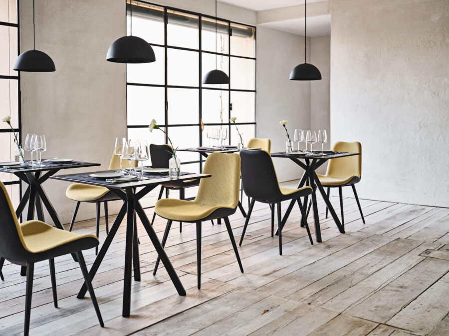 Zona pranzo in loft con tavoli neri, sedie gialle e lampade a sospensione